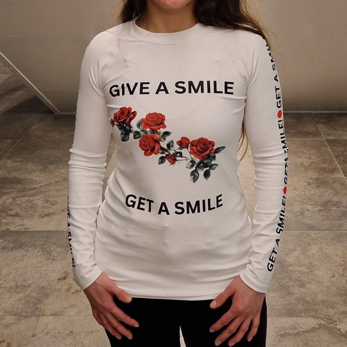 Person wearing a white long sleeve rash guard with floral designs and text in an indoor setting